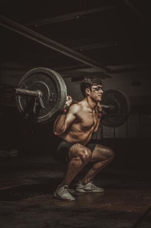 Male lifter demonstrating deep squat barbell technique fixes for beginners with loaded bar on shoulders showing proper stance and knee tracking
