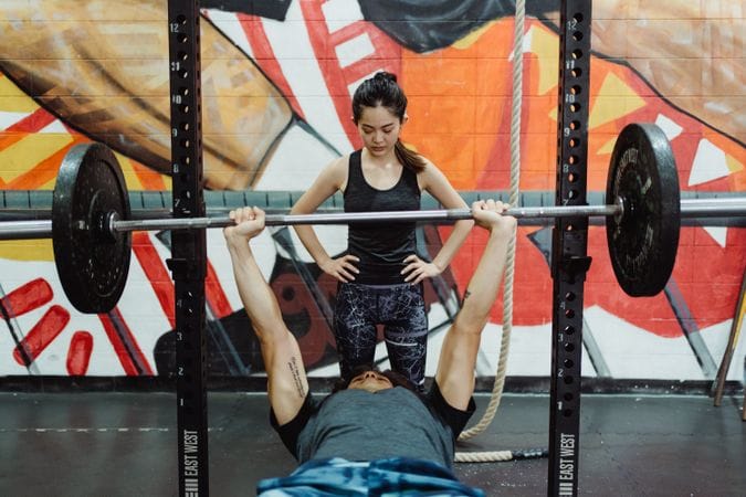 Beginner lifter practicing bench press barbell technique fixes for beginners under supervision in gym showing proper grip and scapular position